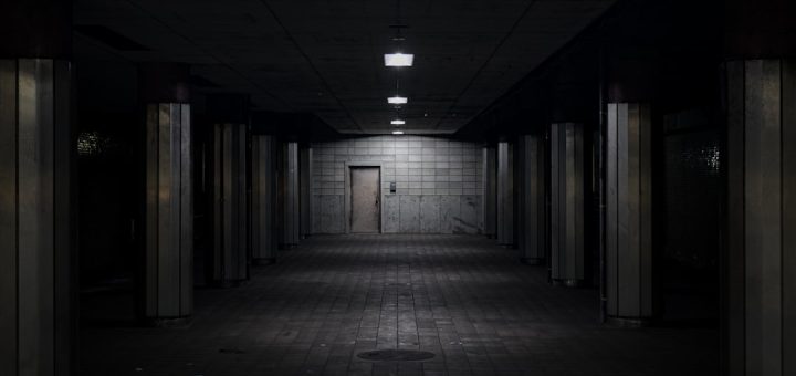 Dark, empty underground tunnel with dim lights and a door.