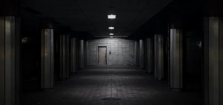 Dark, empty underground tunnel with dim lights and a door.