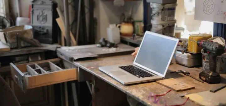 From above of modern laptop laying at table among different tools and equipment in workshop
